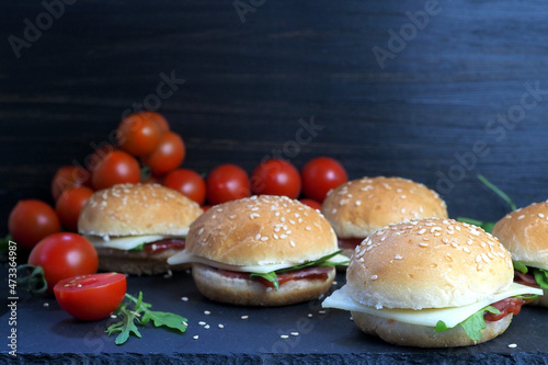 Buns with cheese, ham, herbs and ketchup. Fresh cherry tomatoes and rukula salad. On a dark vintage background photo