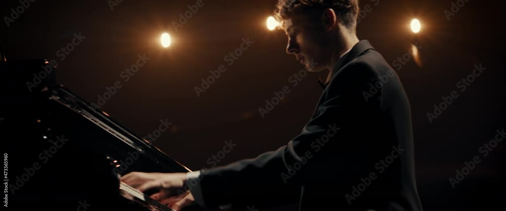 PORTRAIT of Young 20s aspiring musician playing grand piano on a stage of a huge concert hall. Shot with 2x anamorphic lens