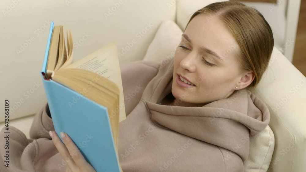 The student is studying during quarantine. A cute girl lies on the couch and reads an interesting book. The student is studying during quarantine. A cute girl lies on the couch and reads an interesting book.