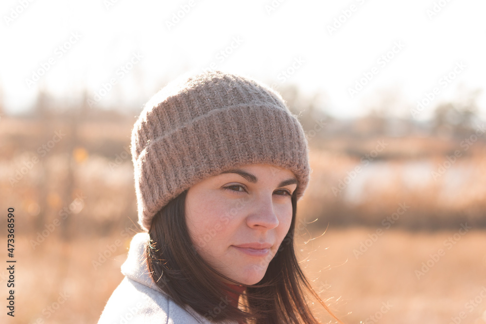 A serious girl in a knitted hat stands against a background and a coat against the backdrop of an autumn pale river landscape A serious girl in a knitted hat stands against a background and a coat against the backdrop of an autumn pale river landscape