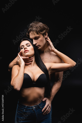 sexy young woman in bra and jeans embracing muscular man isolated on black. © LIGHTFIELD STUDIOS