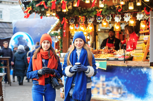 Two friends met at the Christmas market and are walking. Women drink coffee on the street and socialize.