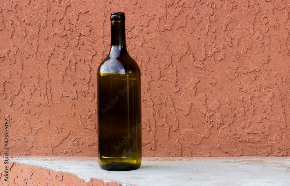 Empty 1.5 liter wine bottle against a terracotta colored concrete wall