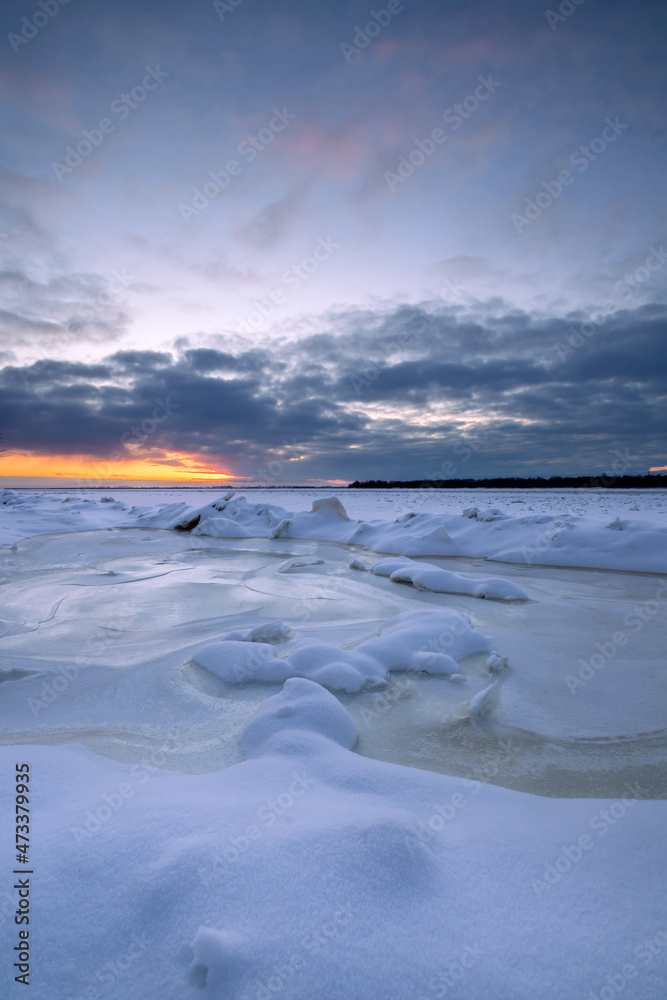 Fototapeta premium Beautiful winter sunset over the frozen river. Ice with sunset reflections in the foreground