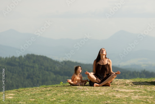 Mother in pose of lotus in mountains with little daughter.