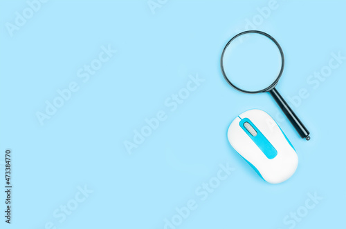 Magnifying glass and computer mouse on blue background
