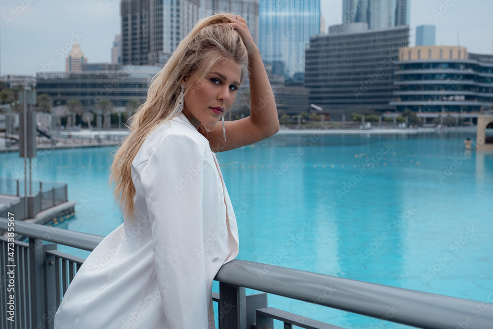 Young beautiful blonde woman enjoying view of Dubai downtown, waiting for famous dancing fountain show. Enjoying travel in United Arabian Emirates. Vacation and sightseeing concept