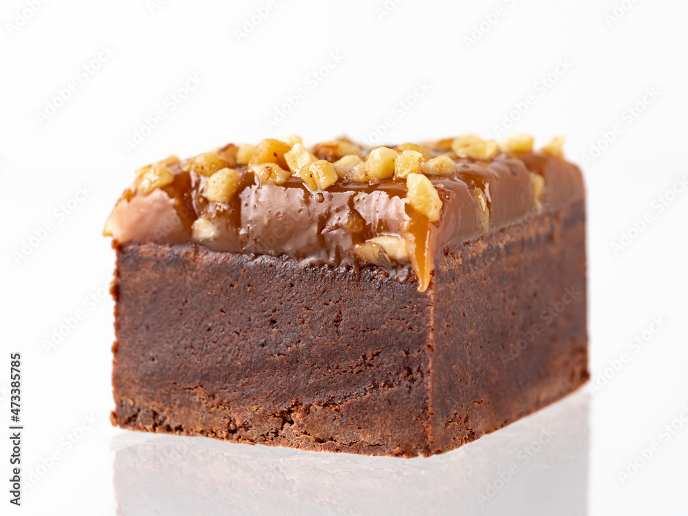 Chocolate brownie cake piece isolated on white. Bite size moist brown chocolate brownie with caramel and peanut topping, isolated on white background with clipping path.