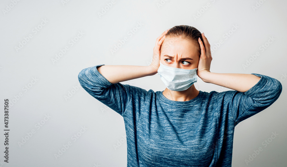 Caucasian masked woman holds her head in panic on white background with copy space. World viral pandemic. Corona virus concept.