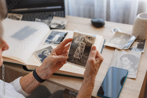 Senior woman is looking her own old photos at home. Elderly woman has got smile while remembering how young and beatiful she was. Selective focus.