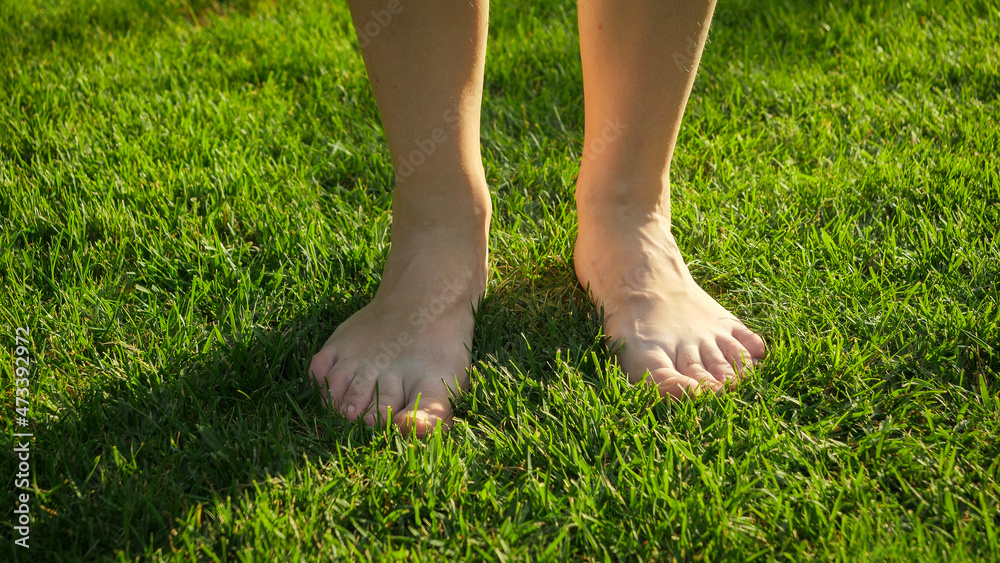 Closeup of female bare feet standing and enjoying fresh green grass at hot summer day. Concept of healthy lifestyle, freedom and relaxation in nature.