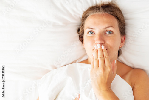 Young woman lies in bed and covers her mouth with her hand. Womens secrets concept