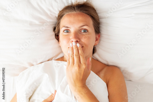 Young woman lies in bed and covers her mouth with her hand. Womens secrets concept