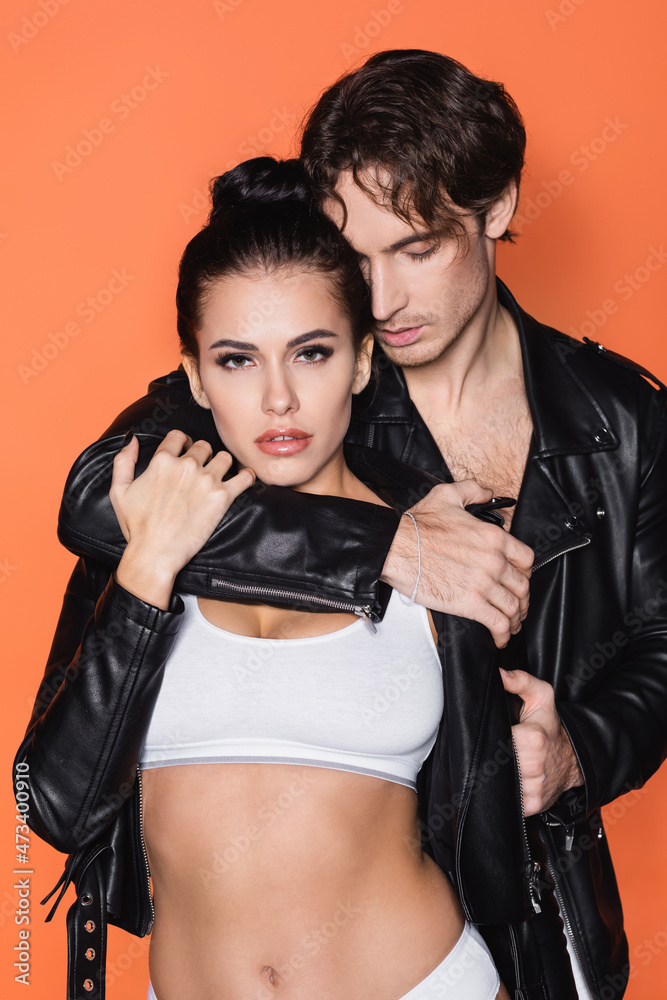 man hugging young woman in black leather jacket isolated on orange. man hugging young woman in black leather jacket isolated on orange.