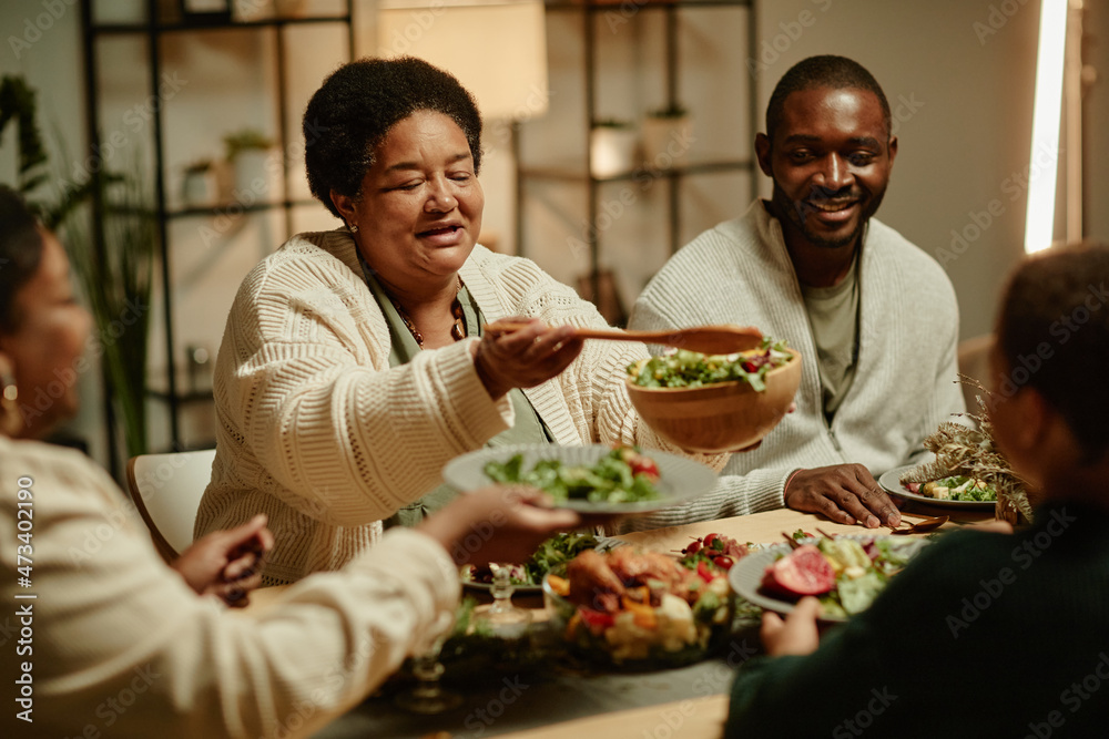 Portrait of smiling African-American grandmother serving food while celebrating Thanksgiving with big happy family at dinner table Portrait of smiling African-American grandmother serving food while celebrating Thanksgiving with big happy family at dinner table