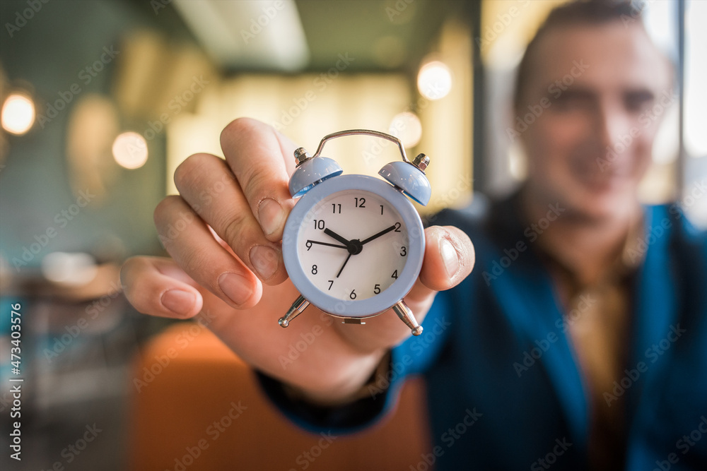 The hand of a smiling businessman man holds the alarm clock. The Concept of Time The hand of a smiling businessman man holds the alarm clock. The Concept of Time