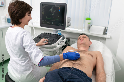 Woman doctor makes heart check of patient man using modern equipment in a cardiology clinic. Female cardiologist is screaning patient heart with ultrasonography, looking at screen. Healthcare concept