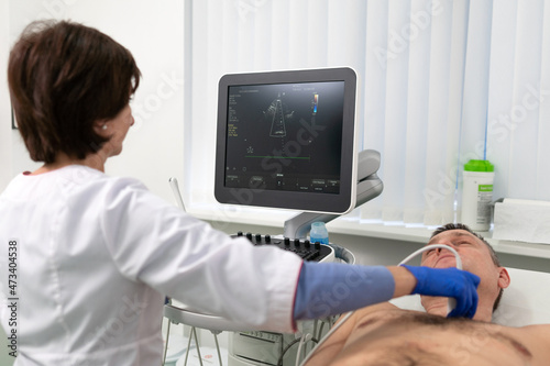 Woman doctor makes heart check of patient man using modern equipment in a cardiology clinic. Female cardiologist is screaning patient heart with ultrasonography, looking at screen. Healthcare concept photo