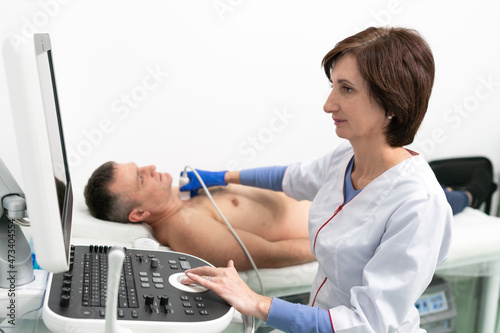 Doctor using ultrasound machine to scan heart of a male patient. Cardiologist makes a patient an echocardiographic test in a clinic. Patient under ultrasound examination in the hospital. 