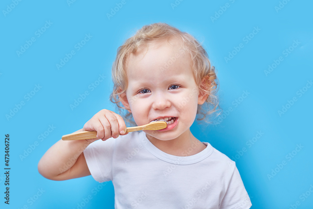 curly-haired girl brushes her teeth with a wooden toothbrush on a blue background with copies space. The concept of recycling and eco friendly curly-haired girl brushes her teeth with a wooden toothbrush on a blue background with copies space. The concept of recycling and eco friendly