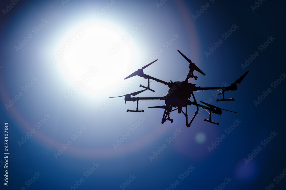 Naklejka premium agricultural drone for fertilizers and pesticides silhouette in front of the sun.