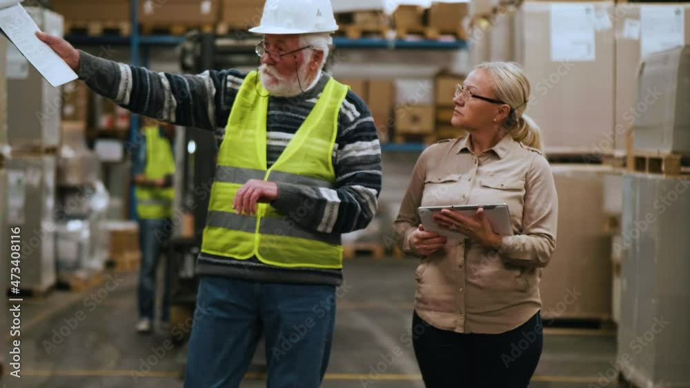 Female manager and old worker checking goods in warehouse using digital tablet. Industry and supply chain management concept. Slow motion Female manager and old worker checking goods in warehouse using digital tablet. Industry and supply chain management concept. Slow motion