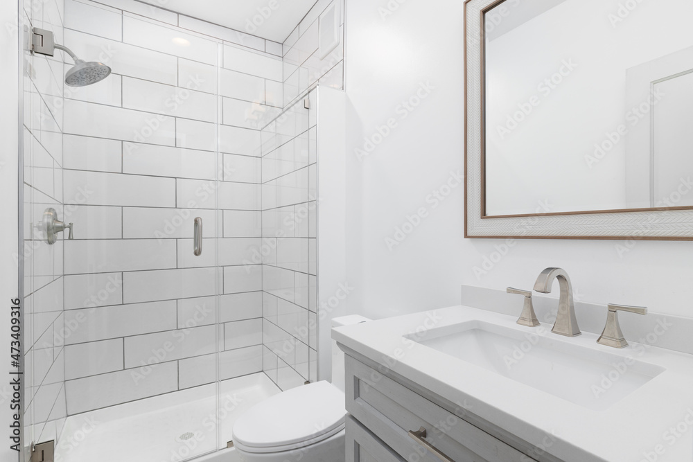 A white bathroom with a grey vanity cabinet, white marble countertop ...