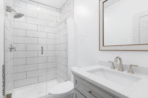 A white bathroom with a grey vanity cabinet, white marble countertop, and a shower with large rectangle tiles.