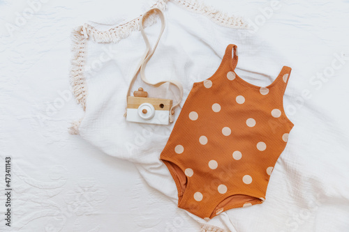 Summer concept. Baby girl swimsuit on white background, ramp leaf and wooden camera toy. Holiday baby concept photo