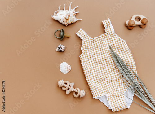 Cute retro swimsuit for baby girl with seashells and beach accessories on brown background. Summer holiday concept. Top view, flat lay photo