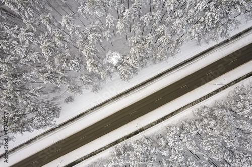 Aerial view of asphalt highway leading through frosty winter forests and groves covered with hoarfrost and snow. Drone photo of black road line and trees with chill snow in mountains. Christmas theme © Defree