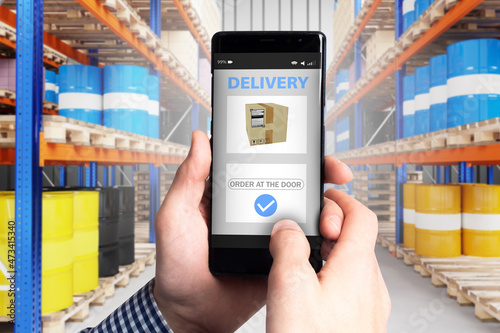 Delivery apps on phone screen. Smartphone with information for courier. Concept is warehouse search application. Advertising of delivery service in phone. Barrels on storage racks. Delivery business