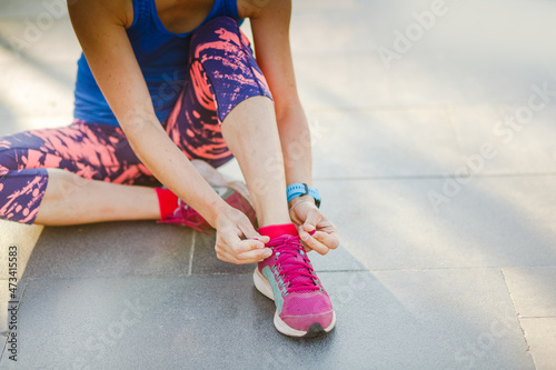fitness woman tie shoelaces on road. Runner sitting on floor on city streets wearing sport shoes. Active woman tying shoe lace before running