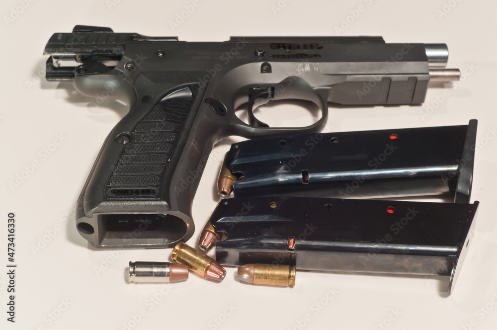 top, view, medium distance of a nine mm hand gun with slide open with two sixteen round -, black magazines and scattered bullets top, view, medium distance of a nine mm hand gun with slide open with two sixteen round -, black magazines and scattered bullets