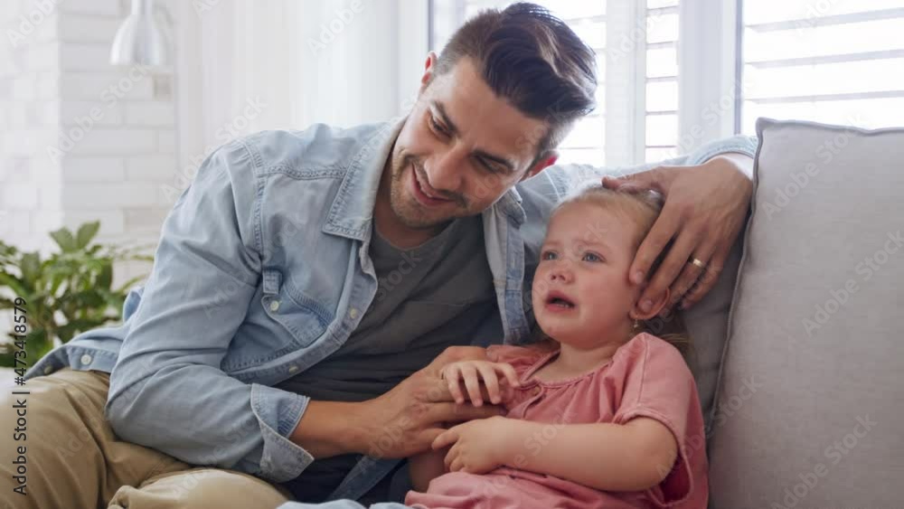 Young father sitting on sofa, holding and calming down his little daughter indoors at home. Young father sitting on sofa, holding and calming down his little daughter indoors at home.