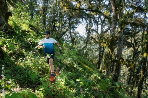 One man running on a trail surrounded by dense forest and vegetation photo