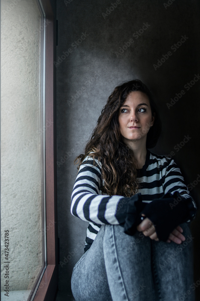 A young girl is resting sitting by a window