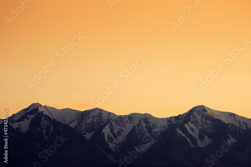 Sunset cloudless sky over gloomy snow-capped mountains.