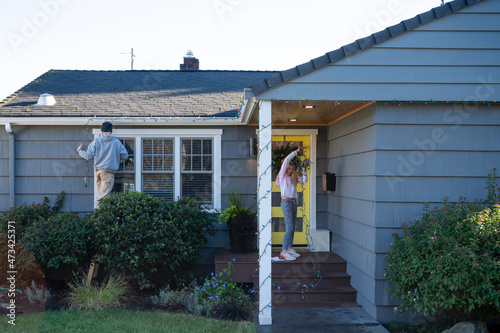 Man and tween girl decorating a residential house with holiday lights photo