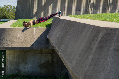Female athlete doing elevated push ups on summer day in concrete photo