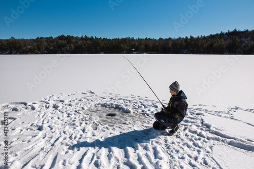 Teen boy ice fishing on a frozen lake in Canada on a winter day. photo