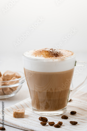 Latte coffee poured in layers with froth and a crispy chocolate top on a light kitchen table. Vertical image with copy space