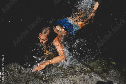 Boy in Bright Trunks Swims and Splashes in a Dark Pool