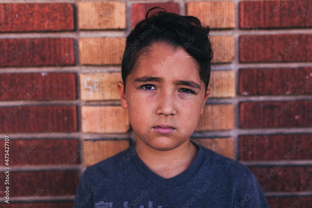 Boy standing in front of a brick wall looking mad. Boy standing in front of a brick wall looking mad.