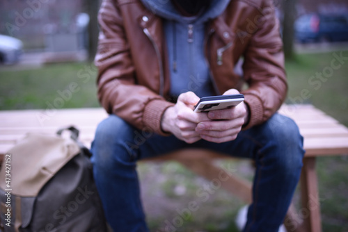 Image focused on the hands of a man with his mobile phone on a wooden bench in a park. photo