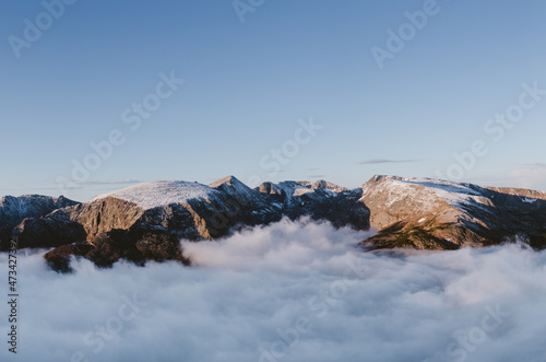 Mountain tops peaking out from soft fluffy clouds below at sunrise photo