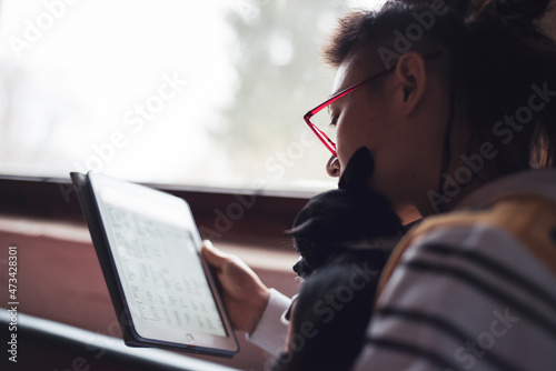 woman in glasses lit by window with small puppy reading spreadsheet photo
