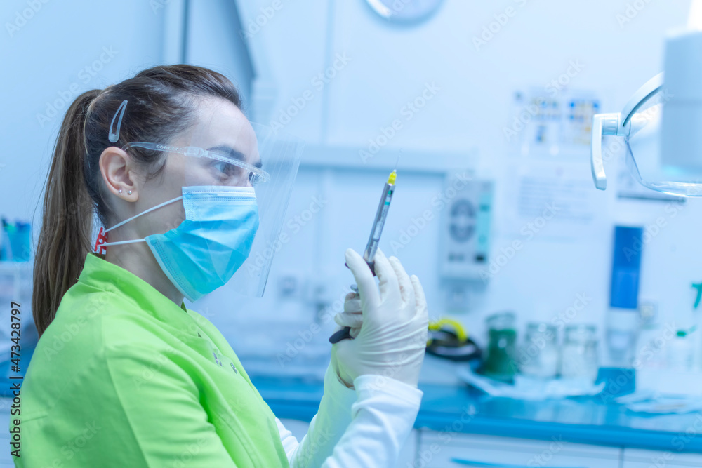 Female dentist preparing the anesthesia syringe wearing a mask Female dentist preparing the anesthesia syringe wearing a mask