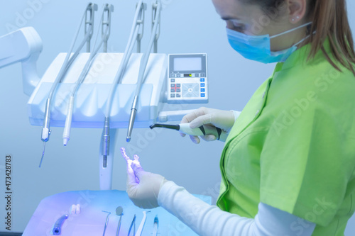 Woman dentist with mask using polymerization lamp in dental clinic photo