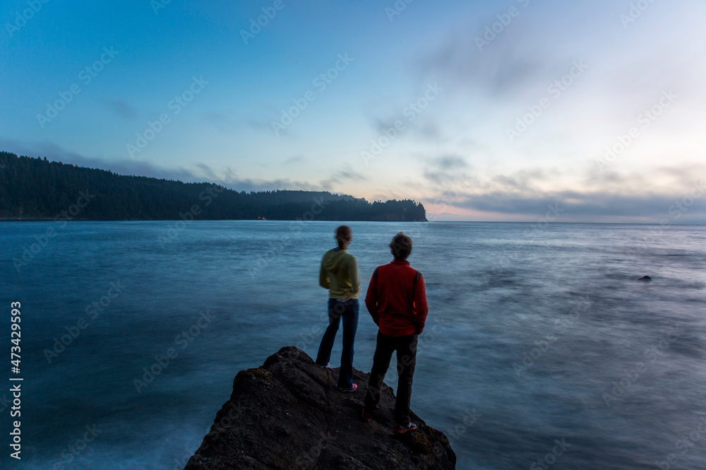 Two young people stand on the edge of a rock formation at dusk near the Strait of Juan de Fuca in Washington. Two young people stand on the edge of a rock formation at dusk near the Strait of Juan de Fuca in Washington.